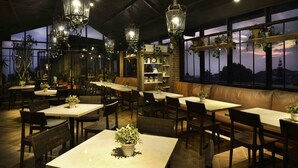Un restaurante con mesas y bancos, faroles colgantes y estantes con plantas.