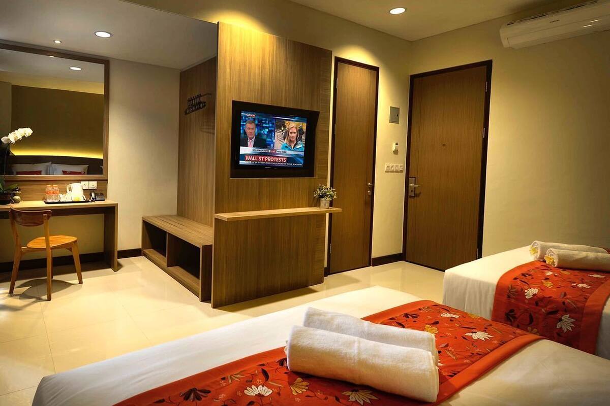 Ein Hotelzimmer mit Fernseher, Schreibtisch, zwei Betten mit Blumenmuster und einem Spiegel.