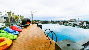Una piscina infinita con terraza de madera, coloridos pufs y vistas a la ciudad.