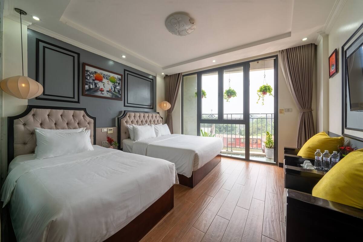 A hotel room with two beds, a balcony with potted plants, and a view of the outside.