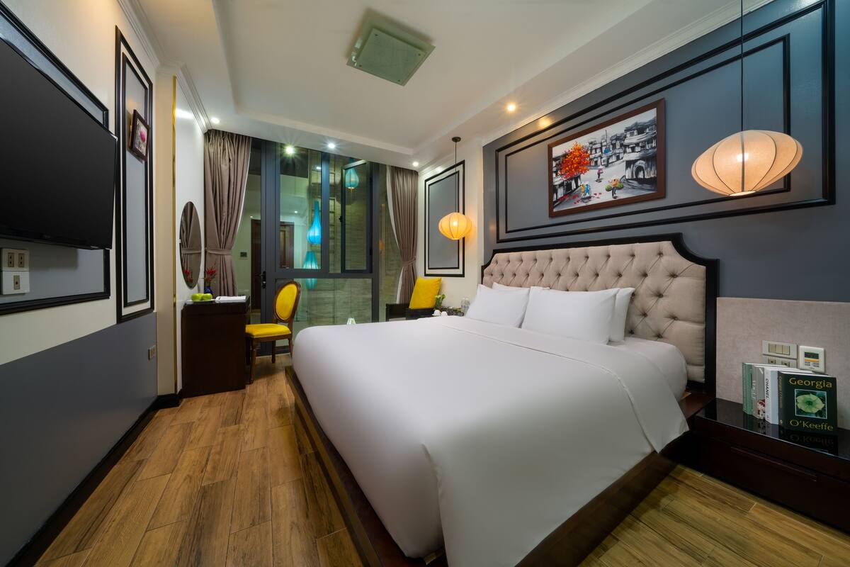 A hotel room with a large bed, a television, a desk with a chair, and a window with curtains.