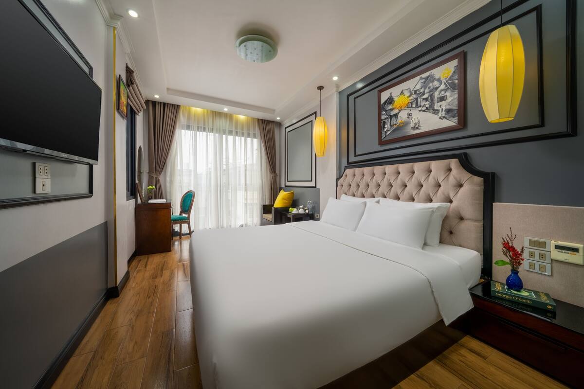 A hotel room with a large bed, a bedside table with a lamp, a chair, and a wall-mounted TV.