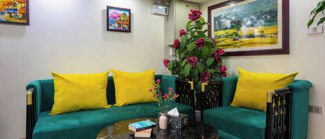 A living room with teal sofas, yellow cushions, a black coffee table, and a large painting on the wall.