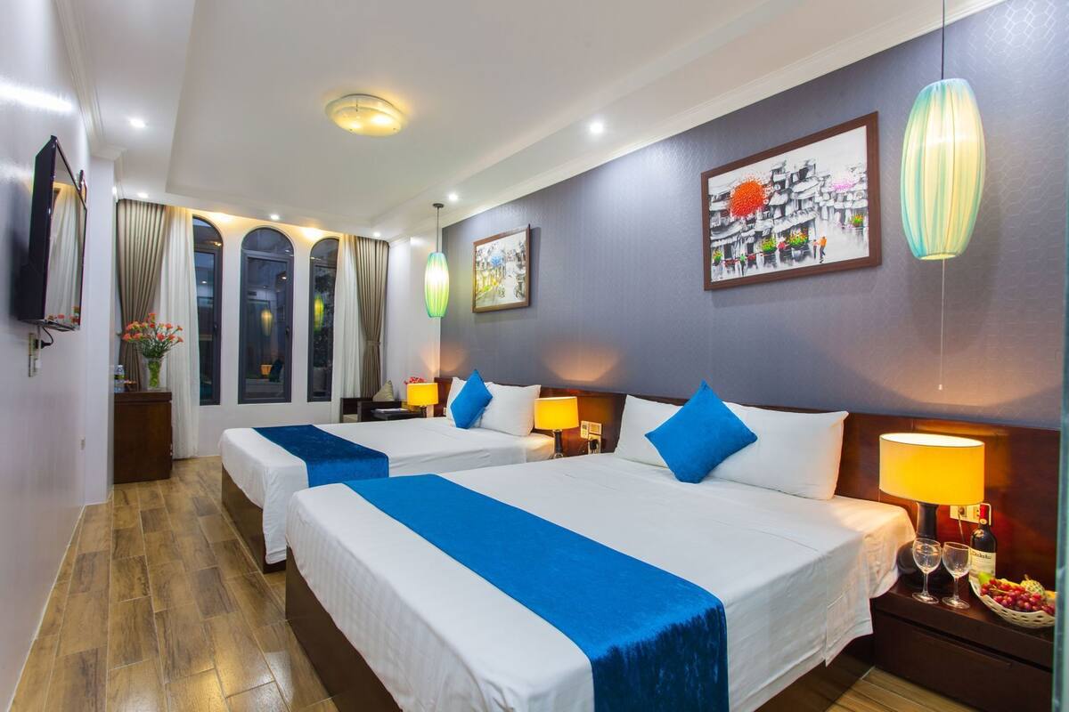 A hotel room with two beds, a TV, a painting, and a window with curtains.