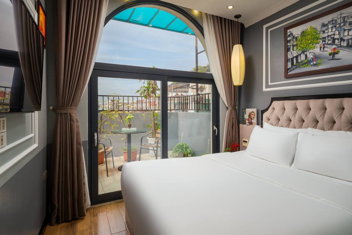 A hotel room with a large bed, a balcony with a view, and a painting on the wall.