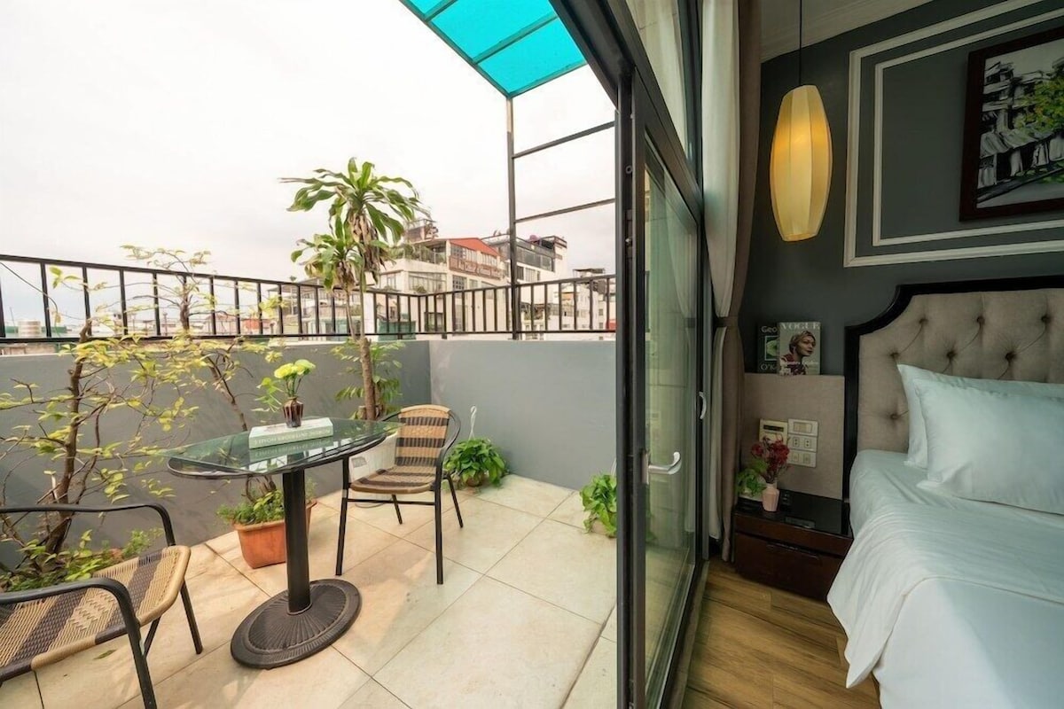 Un balcón con una mesa de vidrio, sillas, plantas en macetas y vistas a edificios.