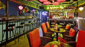 A rooftop bar with wicker furniture, red cushions, and hanging lanterns. - Bella Premier Hotel & Rooftop Skybar (Hanoi)