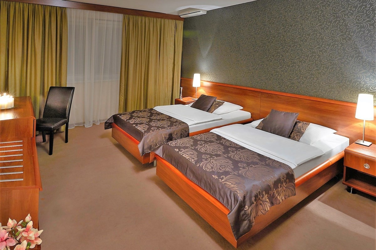 A hotel room with two beds, a desk, a chair, and a lamp.