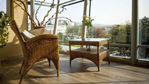 Una silla de mimbre y una mesa en una habitación con ventanas grandes que dan a una vista panorámica de la ciudad.