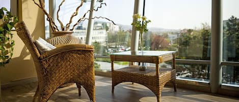 A wicker chair and table in a room with large windows overlooking a cityscape.