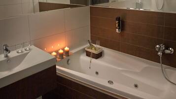 A modern bathroom with a white bathtub, a sink, and a mirror. There are candles on the sink and a basket with toiletries.