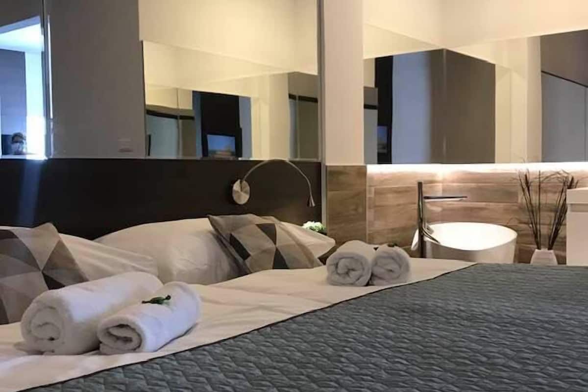 A modern hotel room with a large bed, a round mirror, and a round bathroom vanity.