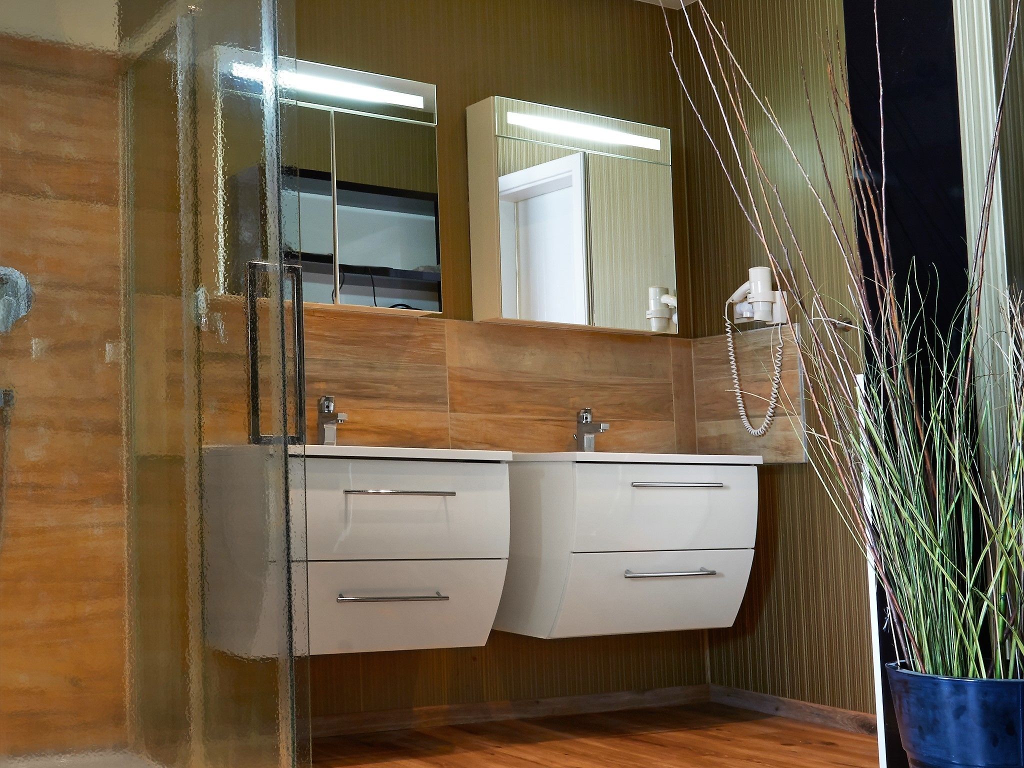 Une salle de bain moderne avec un meuble-lavabo en bois, un grand miroir et une plante en pot.