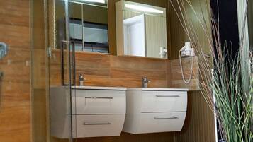 A modern bathroom with a wooden vanity, a large mirror, and a potted plant.