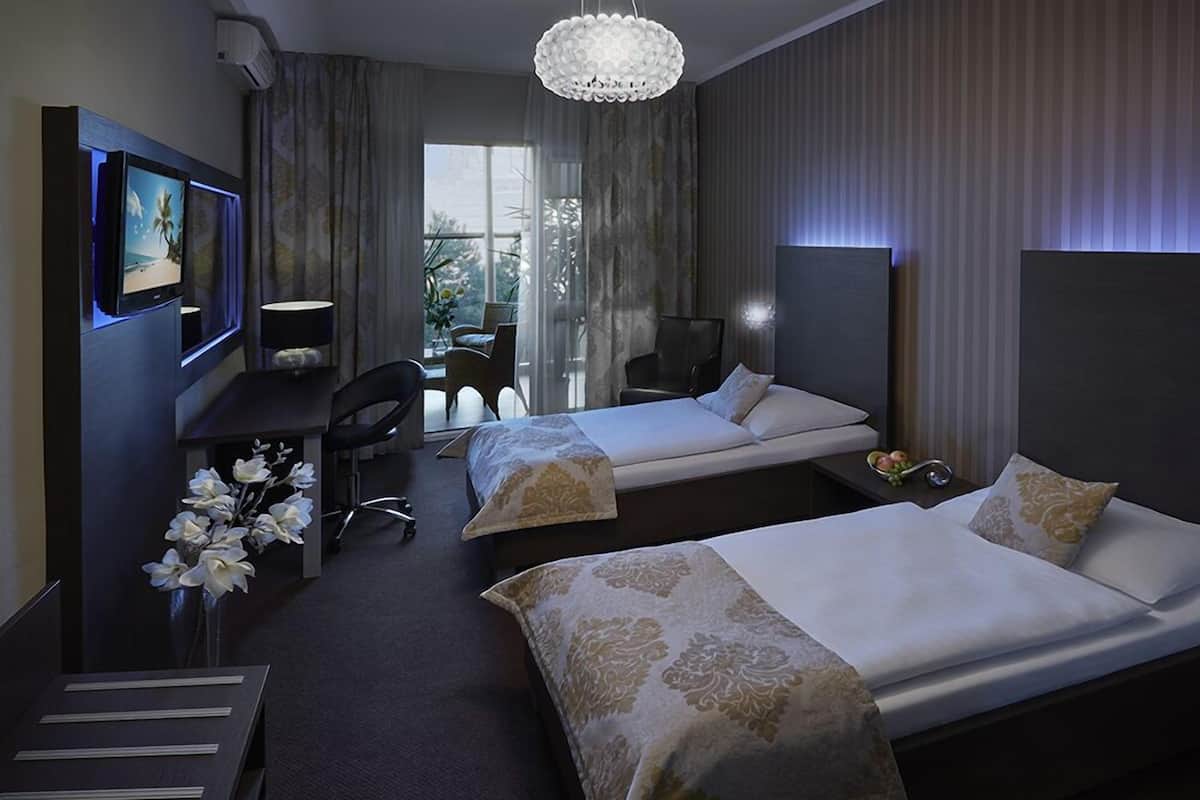 A hotel room with two beds, a desk with a computer, a chair, and a decorative plant.
