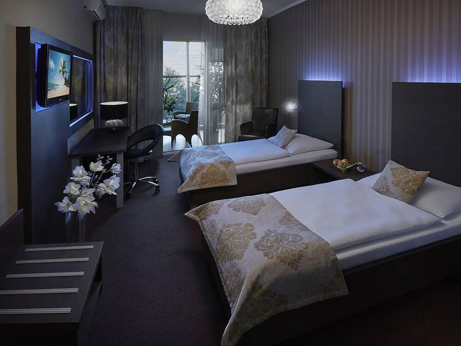 A hotel room with two beds, a desk with a computer, a chair, and a decorative plant.