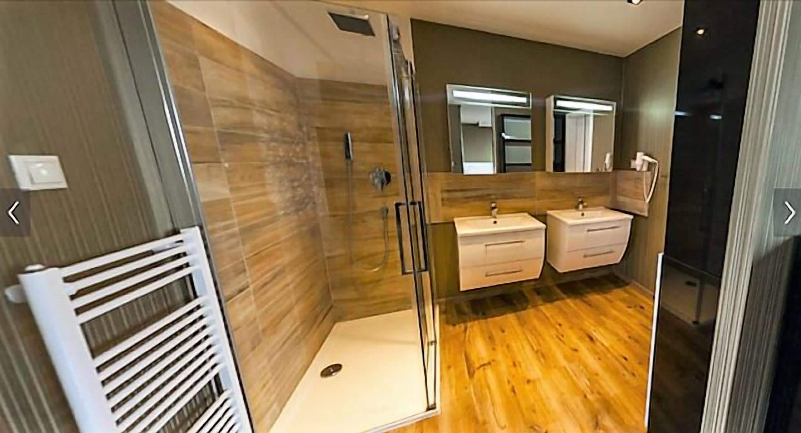 Une salle de bain moderne avec une douche à parois de verre, un plancher en bois et deux vasques avec des miroirs au-dessus.