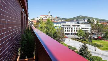 A balcony with a red edge overlooking a cityscape with buildings and a hill with a tower.