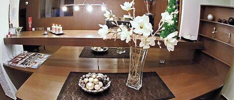 Un espace d’accueil avec un comptoir de réception en bois, un vase rempli de fleurs blanches et un récipient contenant des objets décoratifs.