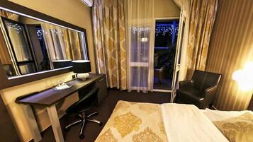 A hotel room with a bed, a desk, a chair, a large mirror, and a view of the outdoors through a sliding door.
