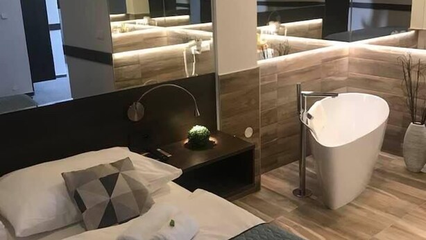 Habitación de hotel moderna con una cama grande, tocador integrado y bañera, además de un espejo amplio.