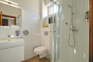 Un baño moderno con ducha envuelta en vidrio, inodoro y lavamanos con espejo superior.