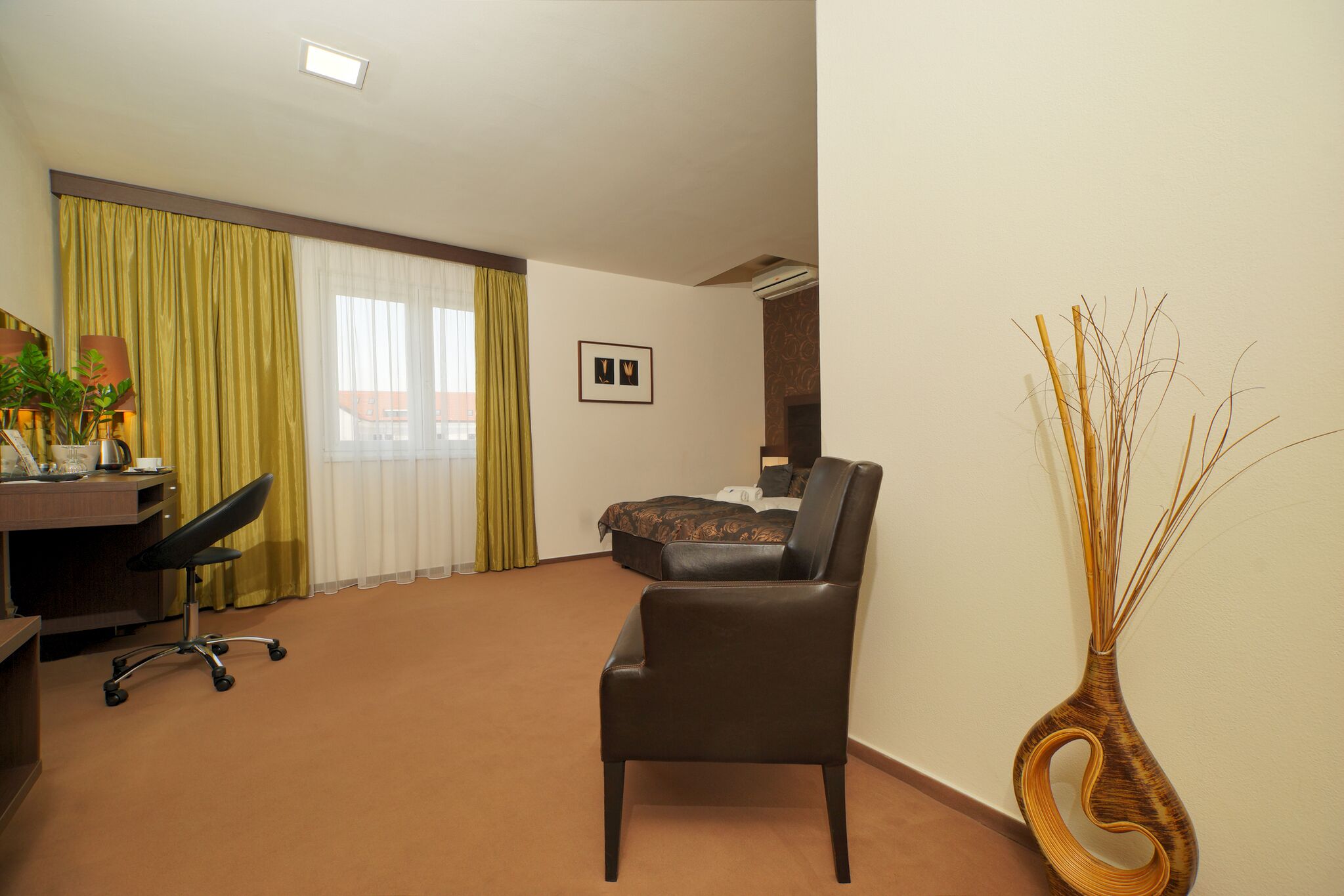 A hotel room with a desk, a chair, a bed, and a decorative vase.