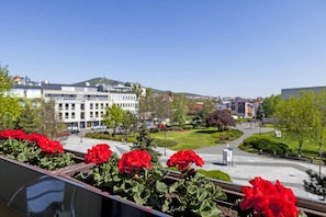 A balcony with red flowers, a view of buildings, and a clear sky.