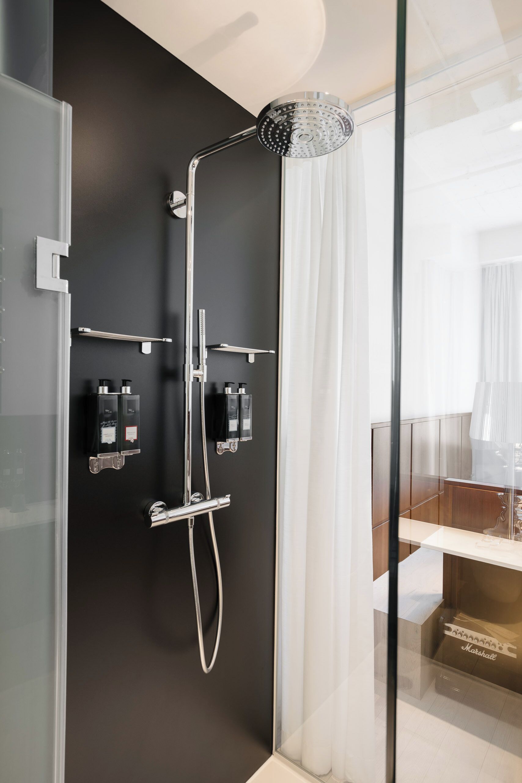 Un baño moderno con cabina de ducha de vidrio, accesorios cromados y pared oscura.