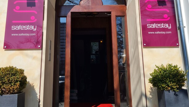 An entrance with a red carpet leading to a door, flanked by two 'safestay' banners, and a large arched window above. - Safestay Berlin Kurfurstendamm (Berlin)