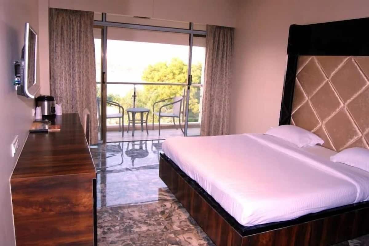 A hotel room with a bed, a desk, a chair, a coffee maker, and a view of the outdoors.