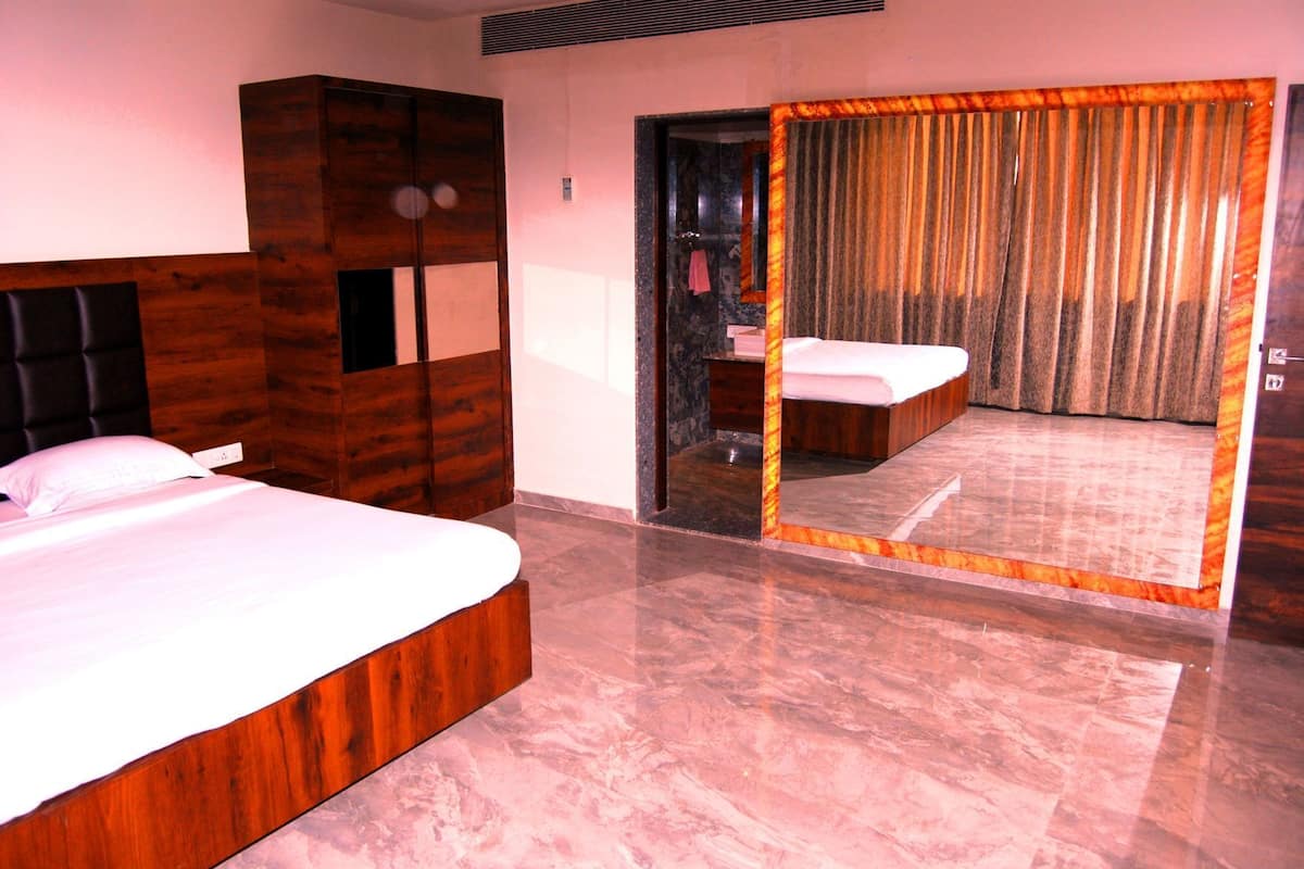 A hotel room with a bed, a wardrobe, a bathroom with a mirror, and a shower area.