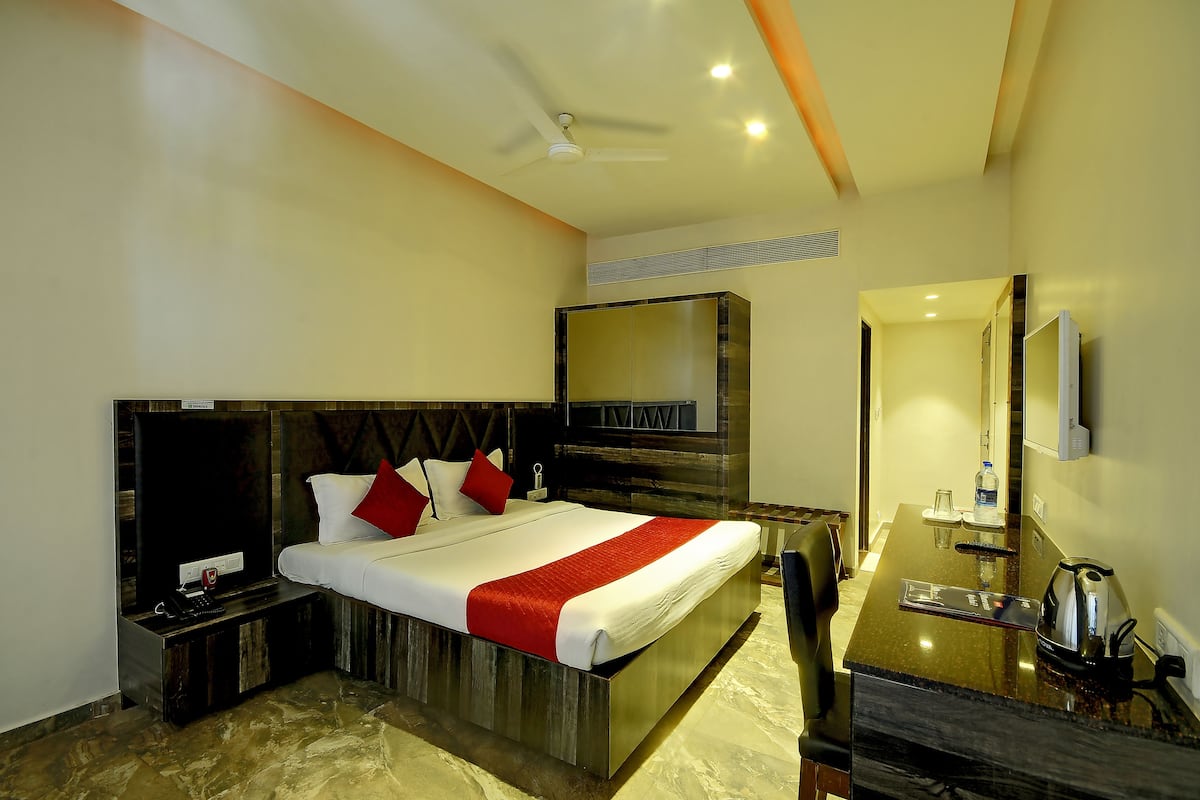 A hotel room with a large bed, a TV, a desk with a kettle, and a mirror.