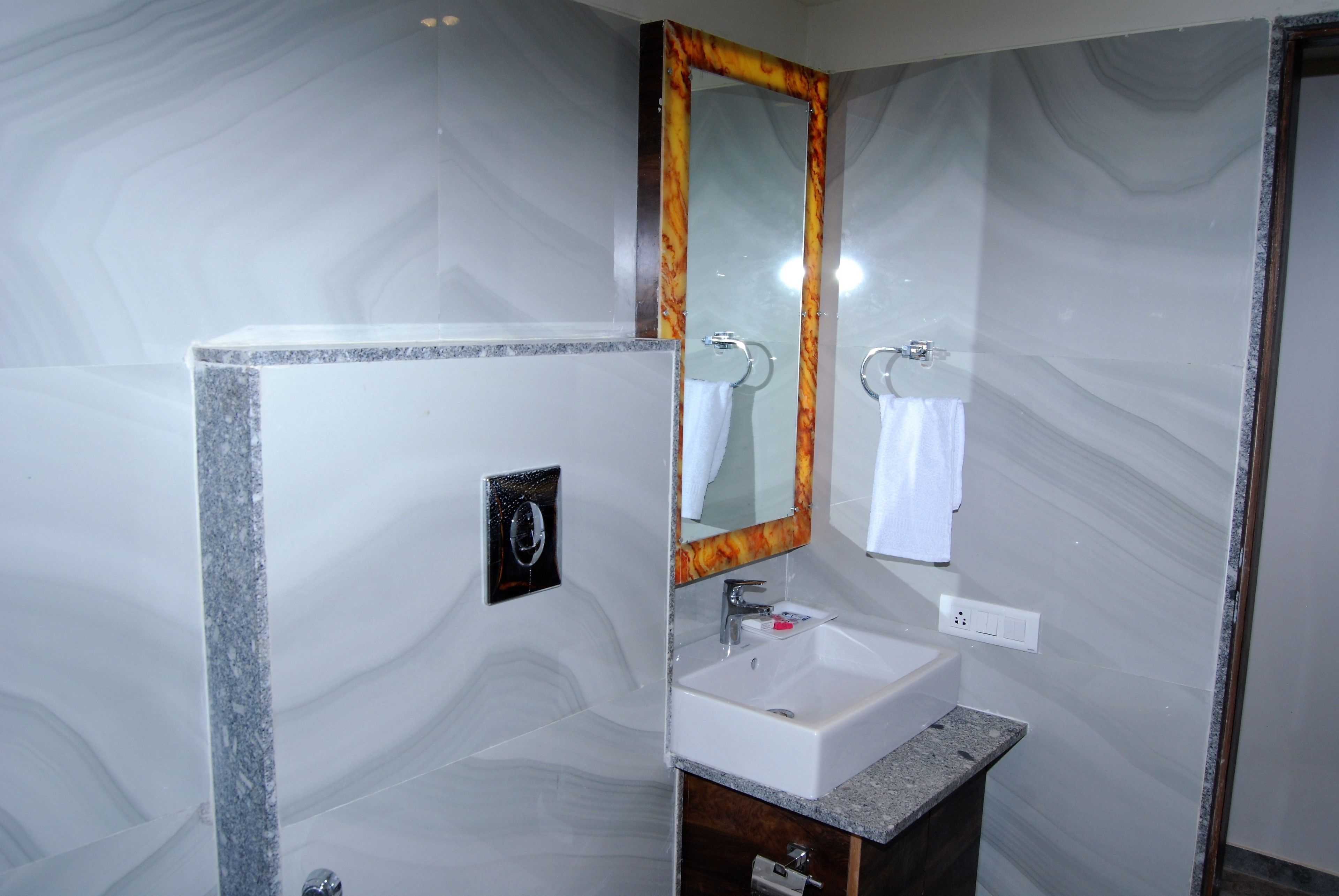 A bathroom with a marble wall, a white sink, a mirror with a wooden frame, and a towel hanging on a ring.