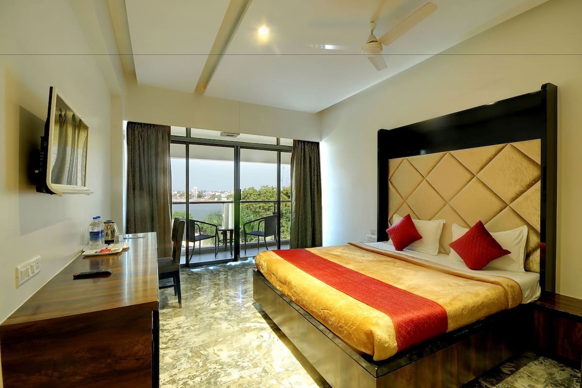 A hotel room with a large bed, a desk with a chair, a TV, and a balcony with a view.