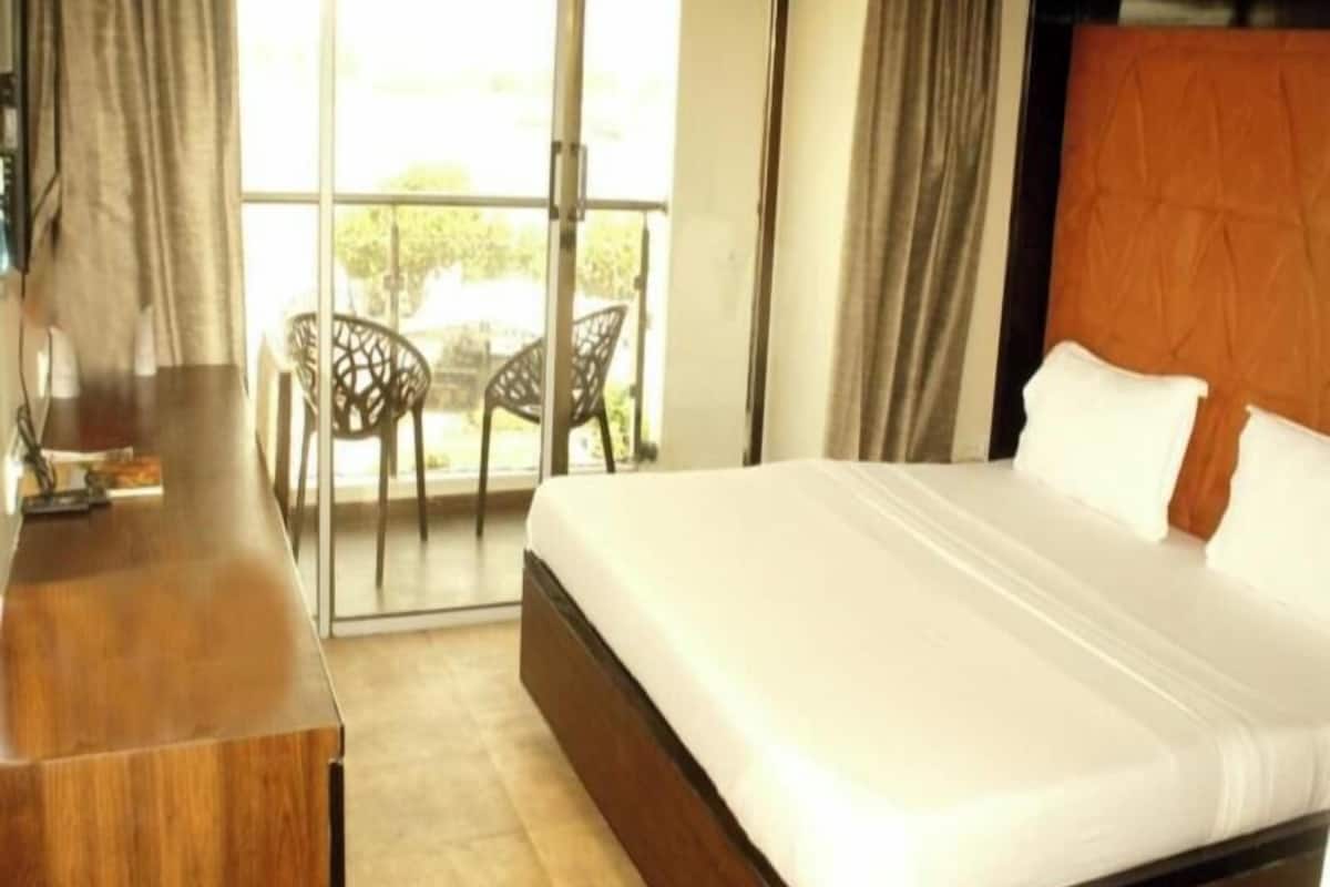 A hotel room with a bed, a desk, and a balcony with chairs.