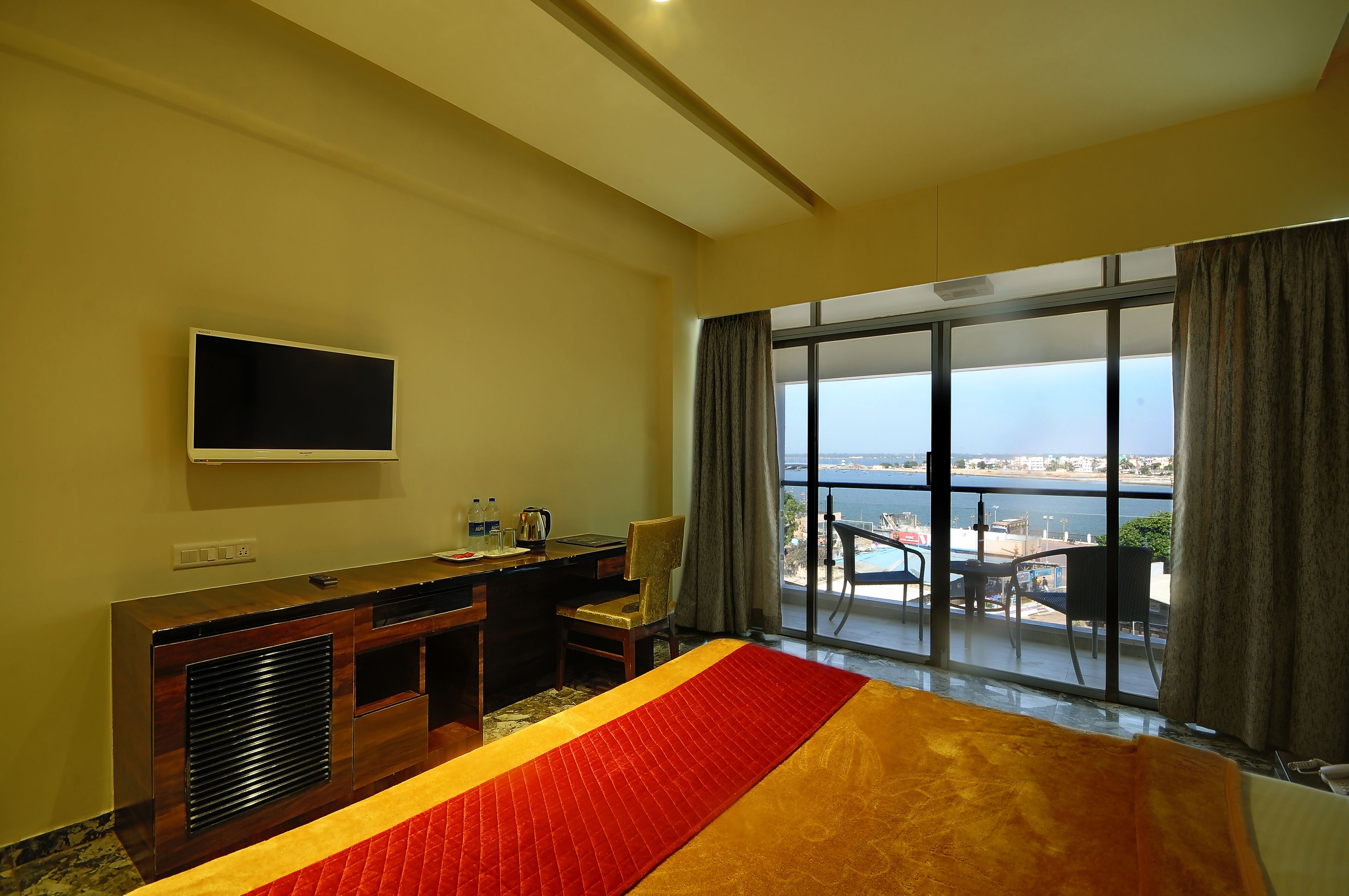 A hotel room with a bed, a desk, a TV, and a balcony with a view of the sea.