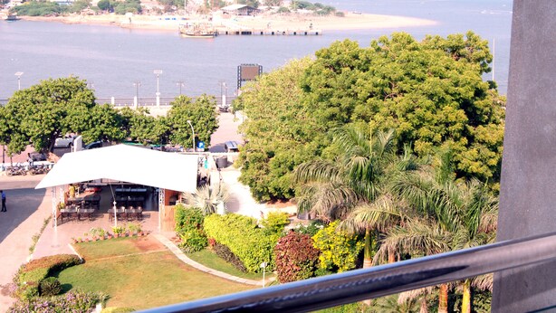 Vista costera con un patio de restaurante con vistas al mar, un estacionamiento y abundante vegetación.