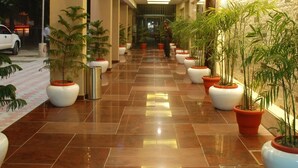 A corridor with potted plants, a tiled floor, and a ceiling with recessed lighting. - Glades Hotel (Mohali)