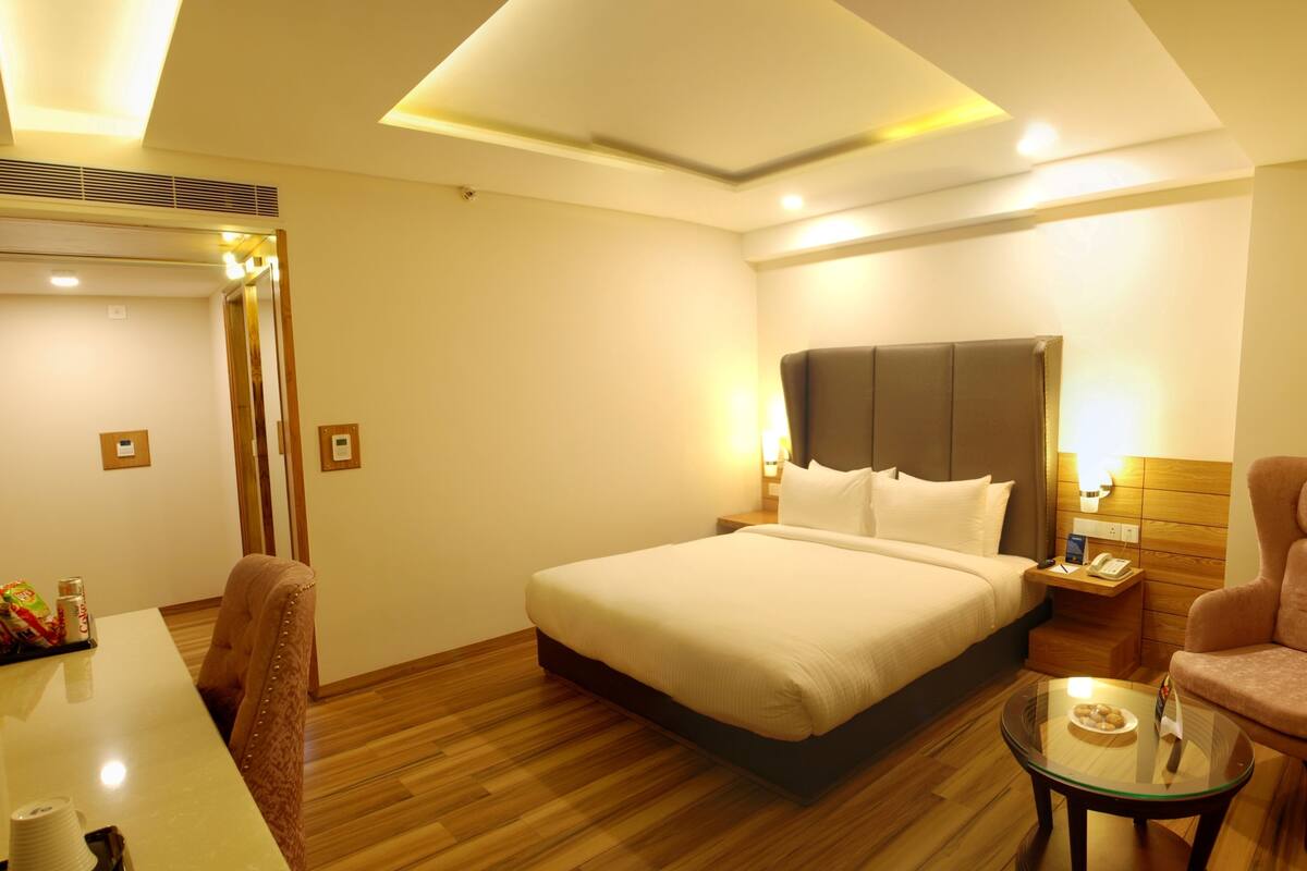 A hotel room with a large bed, a chair, a small table, and a mirror.