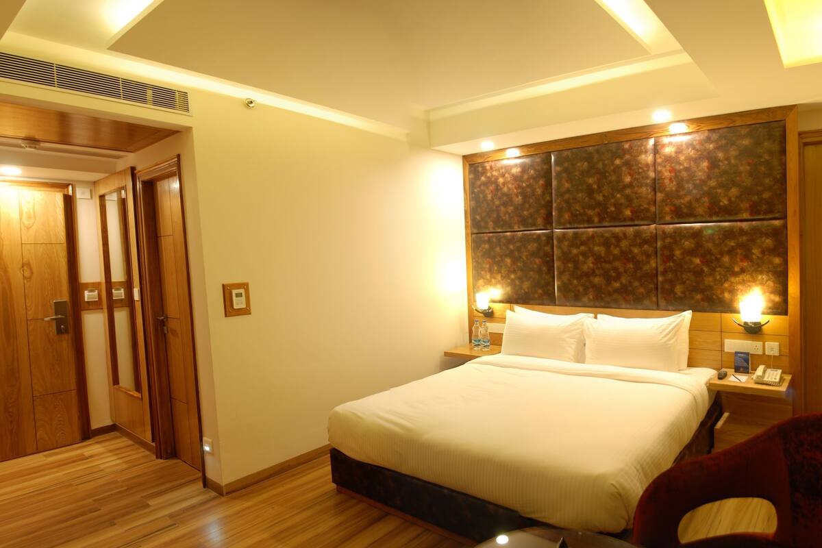 A hotel room with a large bed, wooden wardrobe, and a headboard with a textured design.