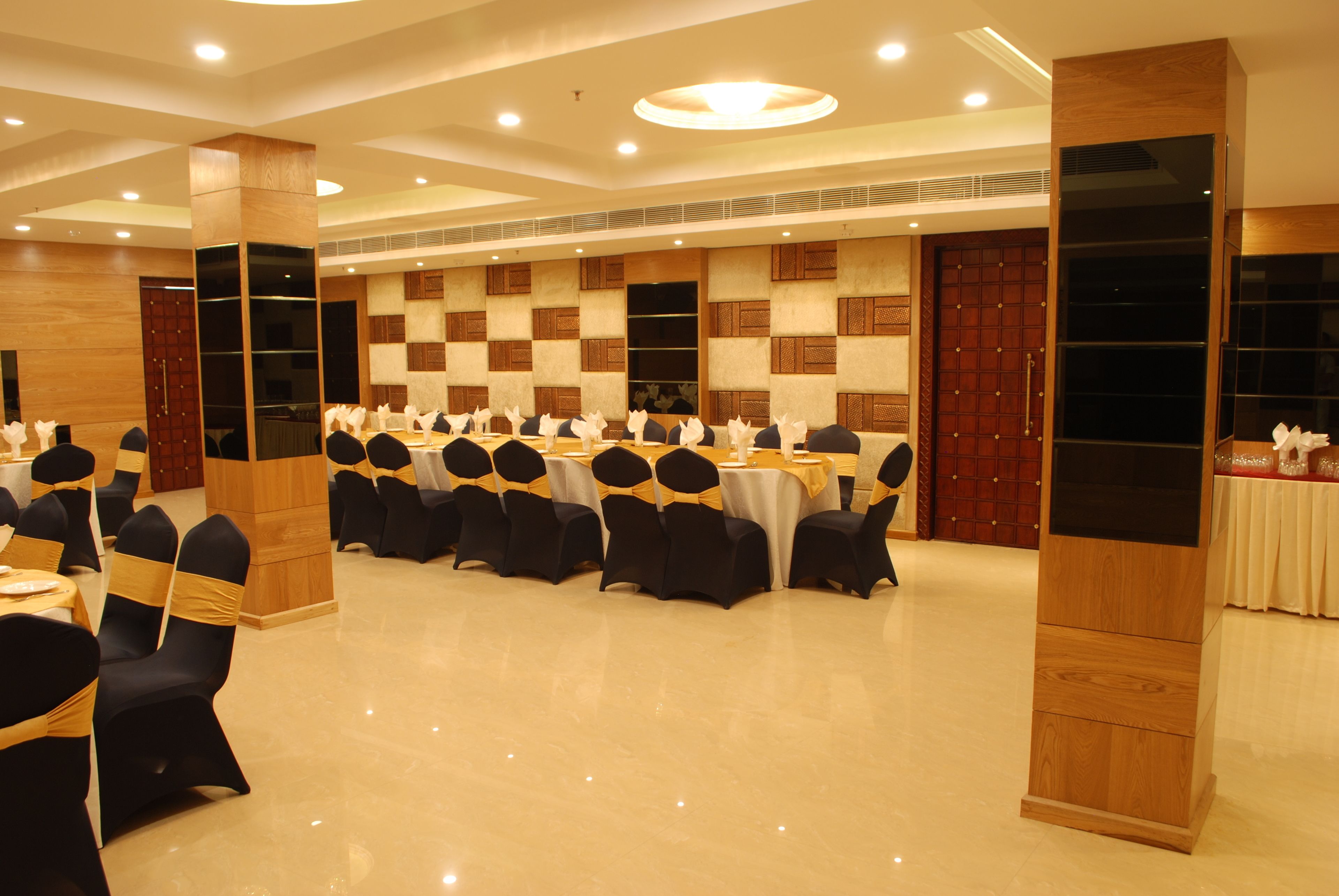 Un salón de conferencias con mesas redondas, sillas negras y un panel de pared de madera.