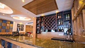 A bar area with a granite countertop, wooden shelving with bottles, and a checkered wall design. - Glades Hotel (Mohali)