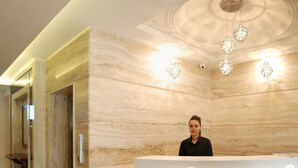 A reception desk with a marble wall backdrop and a chandelier. - Glades Hotel (Mohali)