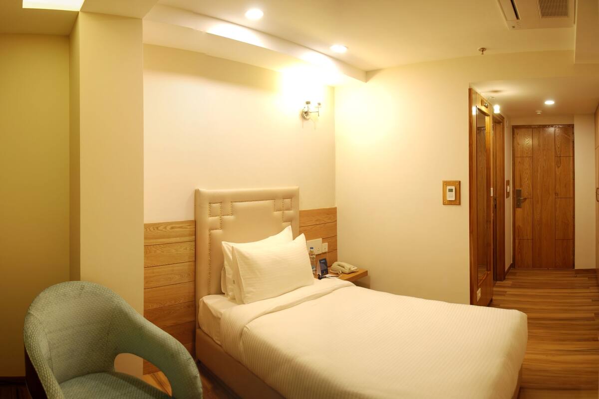 A hotel room with a bed, a nightstand, a chair, and a wooden floor.