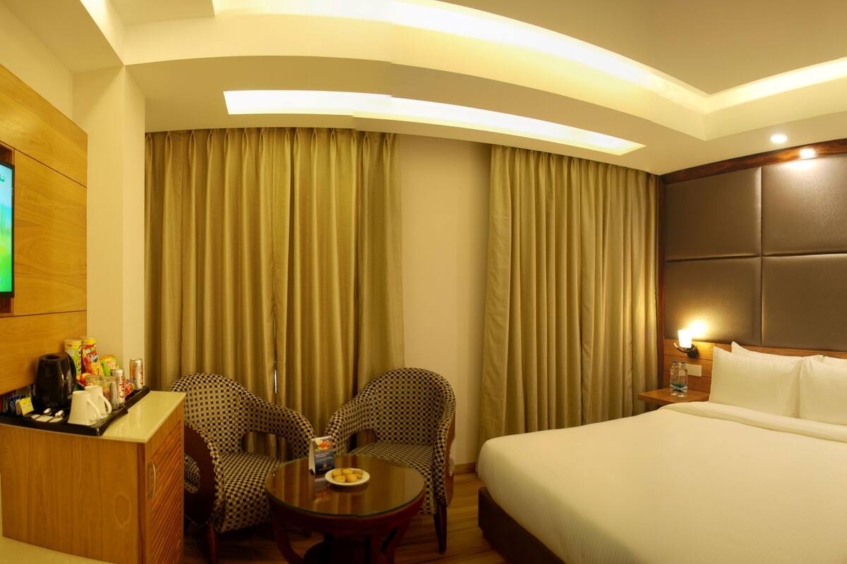 A hotel room with a bed, two chairs, a small table, a desk, and a TV.