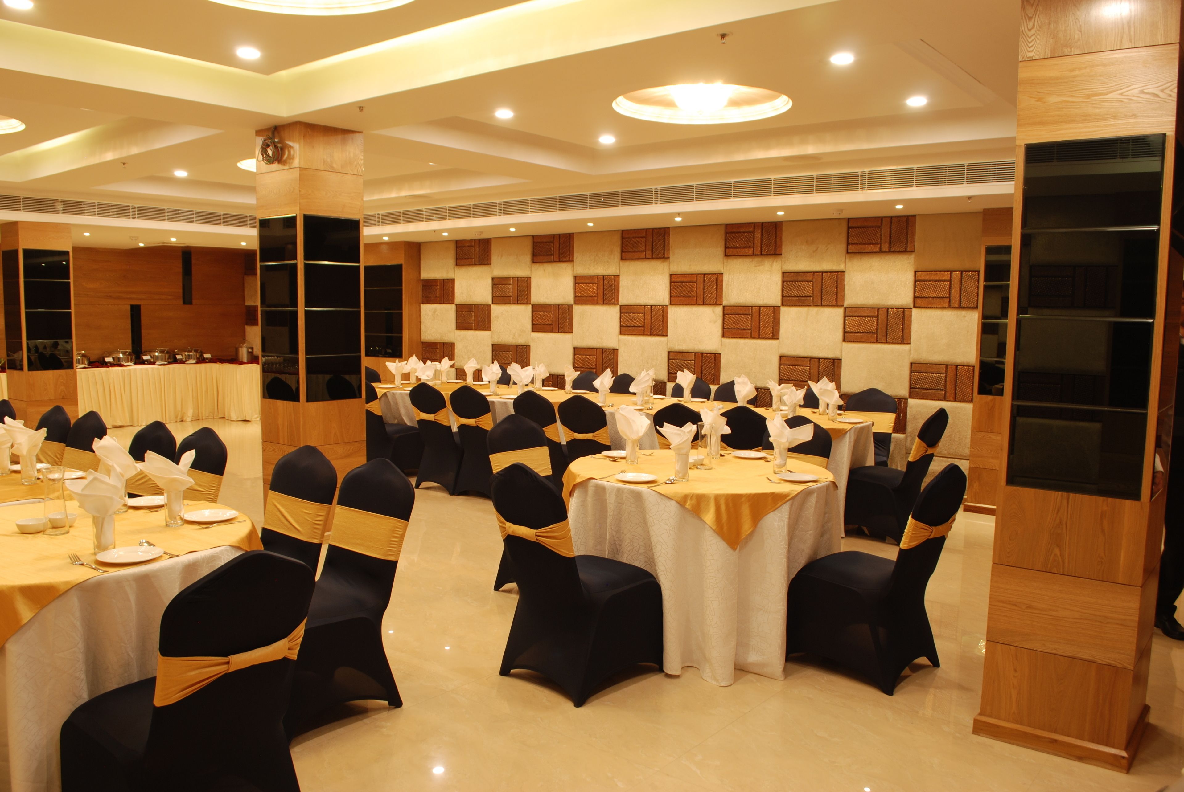 A banquet hall with round tables, black and gold chairs, and a wooden panel wall.