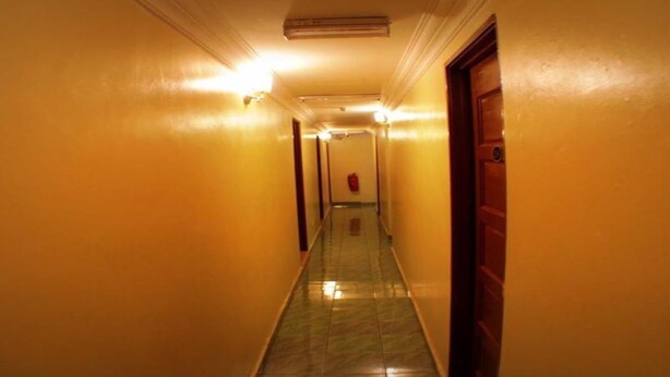 A long, narrow hallway with yellow walls and a green tiled floor, leading to a door at the end. - Taipann Hotel (Klang)