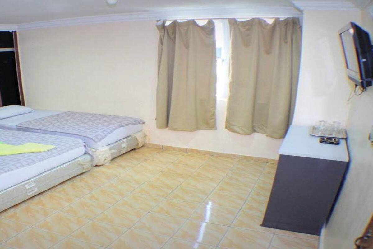 Quarto de hotel pequeno e individual, com duas camas, uma mesa, uma televisão e uma janela com cortinas.