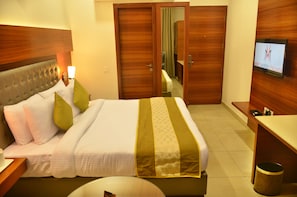 A hotel room with a bed, a television, wooden doors, and a desk. - Mint Hotel Premia (Dera Bassi)